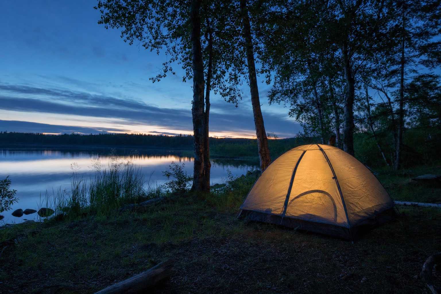 A small tent softly lit from within at dusk beside a calm lake