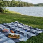 A picnic blanket on the grass by a lake with simple food laid out, no people