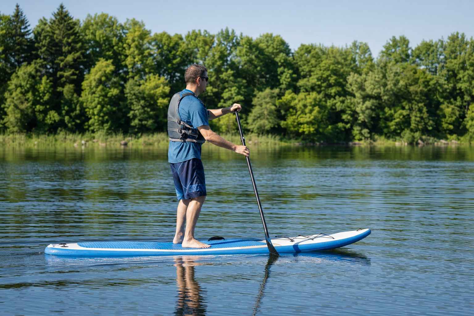 An ordinary adult in a life jacket standing and paddling a stand-up paddleboard on a calm lake