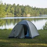 A small dome tent pitched on flat grassy ground set back from a calm lake