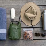 A simple lake-day packing list laid out on weathered wood: towel, sunscreen, hat, water bottle, dry bag and snacks